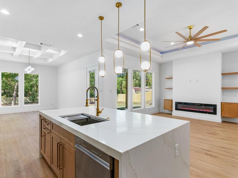 Kitchen featuring light wood-type flooring, a healthy amount of sunlight, stainless steel dishwasher, a kitchen island with sink, and sink