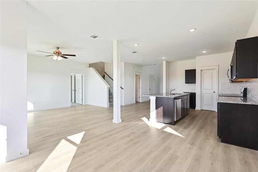 Kitchen with light hardwood / wood-style floors, an island with sink, tasteful backsplash, stove, and ceiling fan