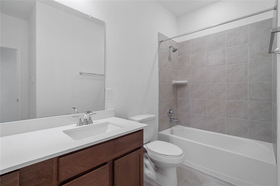 Secondary bath features tile flooring, bath/shower combo with tile surround, stained wood cabinets, beautiful light countertops, mirror, sleek fixtures and modern finishes.