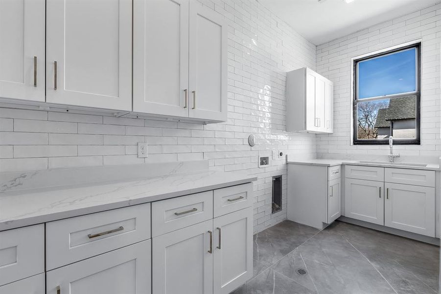 Kitchen featuring white cabinetry, backsplash, sink, light stone countertops, and tile walls