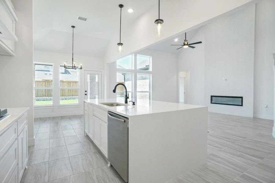 Kitchen with hanging light fixtures, a center island with sink, white cabinetry, stainless steel dishwasher, and sink