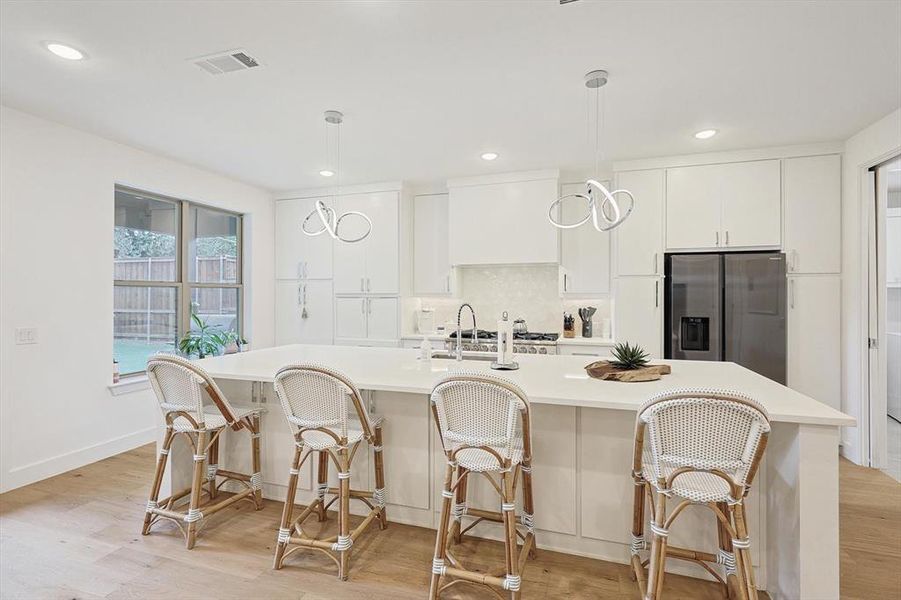 Kitchen featuring light hardwood / wood-style flooring, stainless steel refrigerator with ice dispenser, hanging light fixtures, and an island with sink