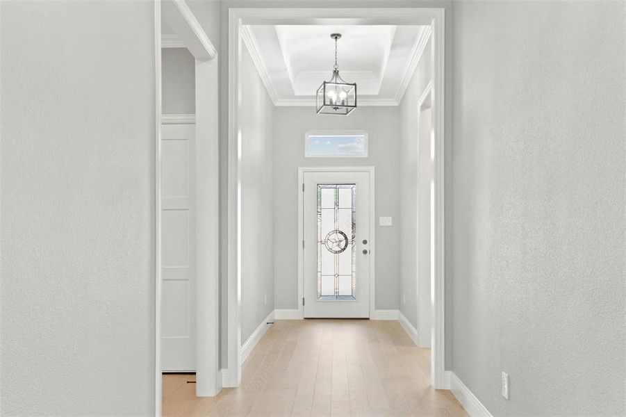 Entrance foyer with ornamental molding, an inviting chandelier, and light hardwood / wood-style floors