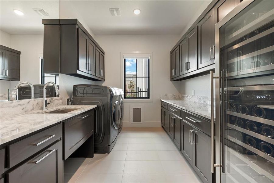 Laundry area featuring light tile patterned floors, sink, washing machine and clothes dryer, beverage cooler, and cabinets