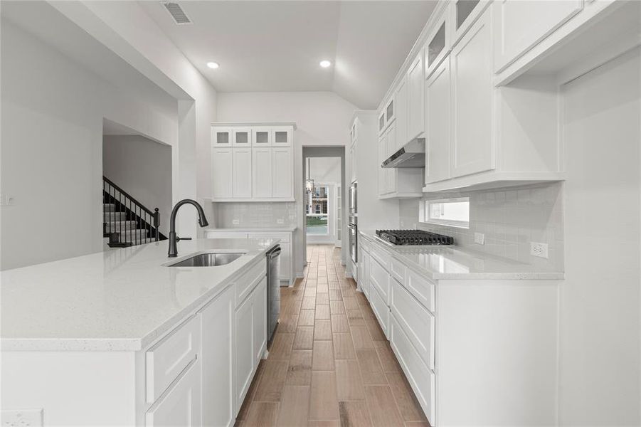 Kitchen featuring tasteful backsplash, white cabinets, sink, range hood, and light stone countertops