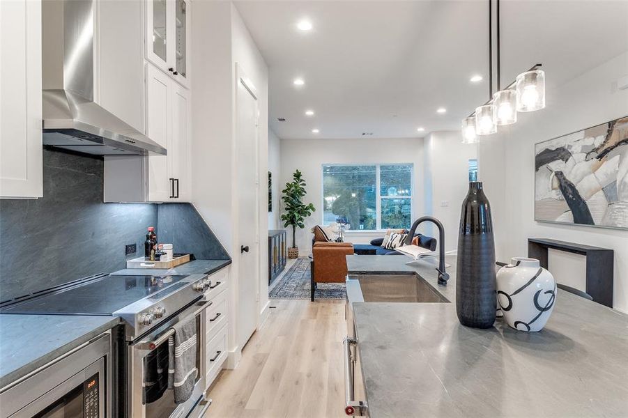 Kitchen with pendant lighting, sink, white cabinetry, wall chimney range hood, and stainless steel appliances