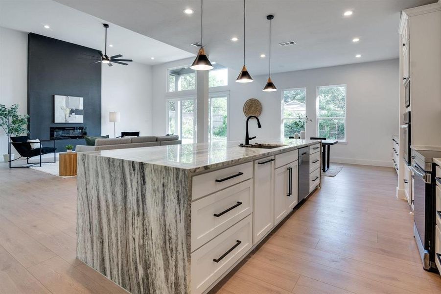 Kitchen with white cabinetry, light wood-type flooring, a kitchen island with sink, pendant lighting, and sink