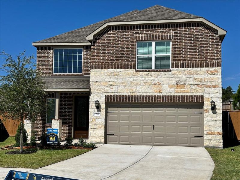 The Sequoia is a beautiful two-story home with a unique two-tone brick and stone design. The home has front yard landscaping and upgraded light fixtures on either side of the garage, with large windows for added curb appeal.