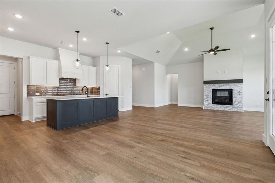 Kitchen with decorative light fixtures, a fireplace, custom range hood, a kitchen island with sink, and ceiling fan