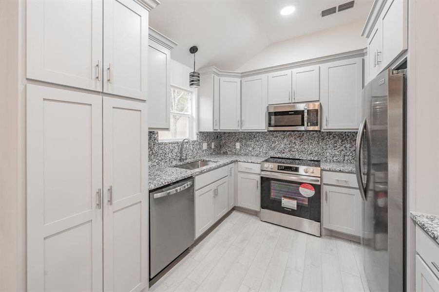 Kitchen with light stone counters, tasteful backsplash, decorative light fixtures, stainless steel appliances, and vaulted ceiling