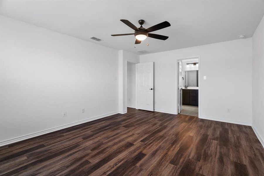 Unfurnished bedroom featuring ceiling fan, connected bathroom, and dark wood-type flooring