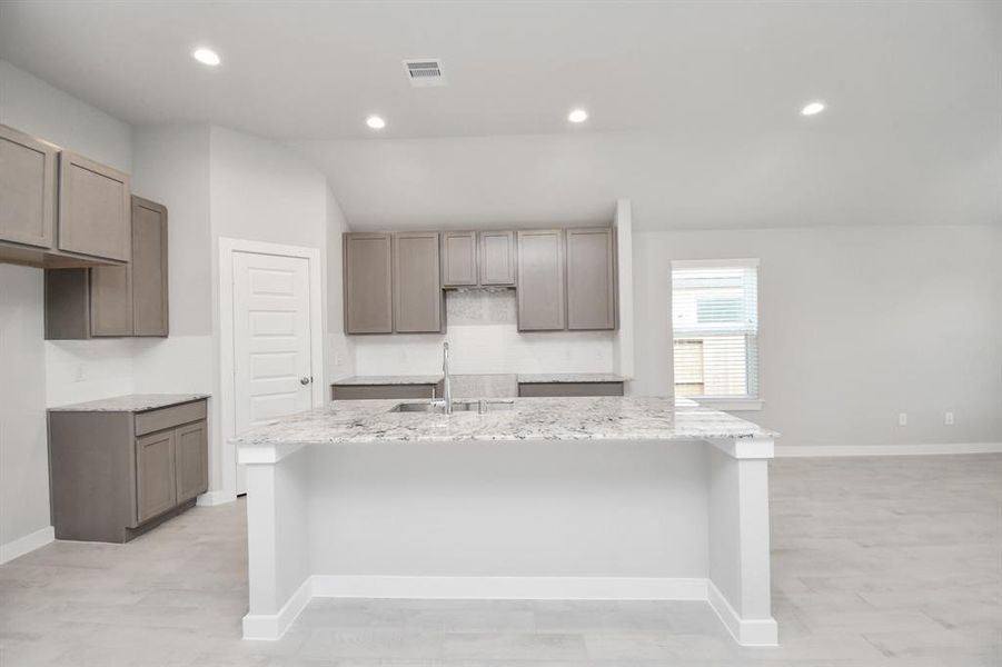Culinary haven, featuring a massive island, granite countertops, a tile backsplash, stainless steel appliances (to be installed), and 42” upper cabinets.