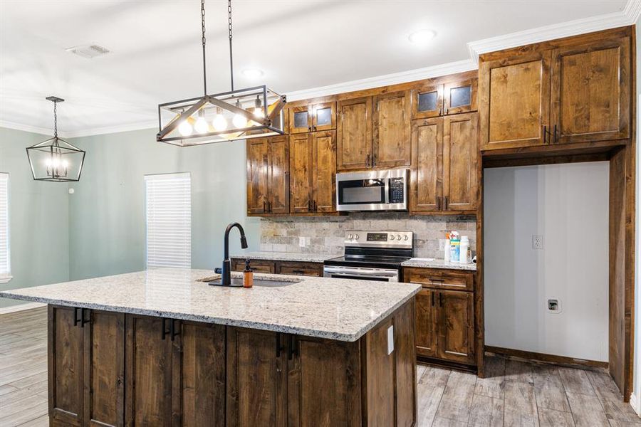 Kitchen with pendant lighting, an island with sink, stainless steel appliances, and sink