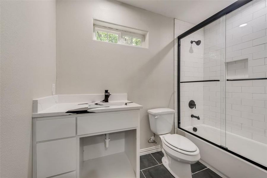 Full bathroom with tile patterned floors, toilet, enclosed tub / shower combo, and vanity