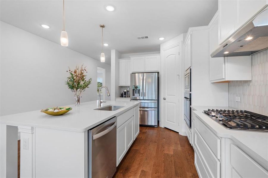 Kitchen with a kitchen island with sink, wall chimney exhaust hood, hanging light fixtures, stainless steel appliances, and sink