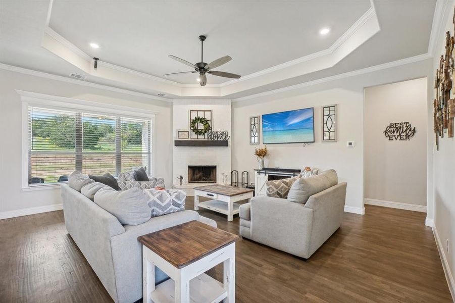 Living room featuring crown molding, a tray ceiling, dark wood-type flooring, and ceiling fan