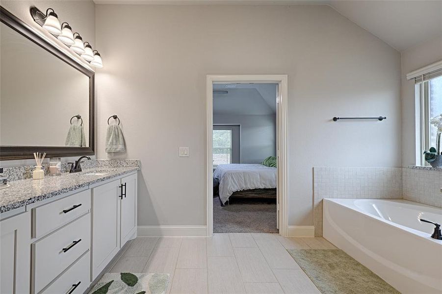 Bathroom featuring vanity, a tub to relax in, lofted ceiling, and tile patterned flooring