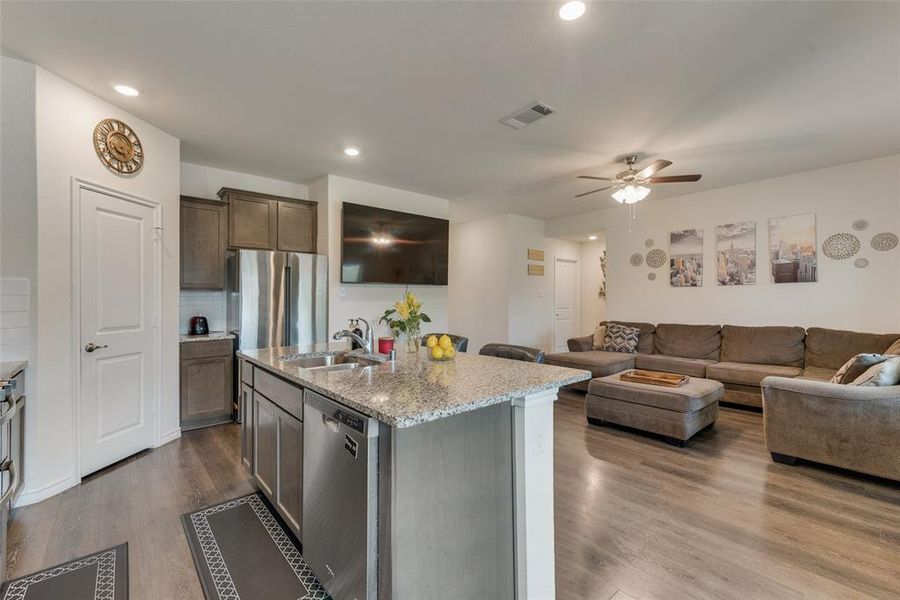 Kitchen featuring wood-type flooring, ceiling fan, decorative backsplash, a center island with sink, and appliances with stainless steel finishes
