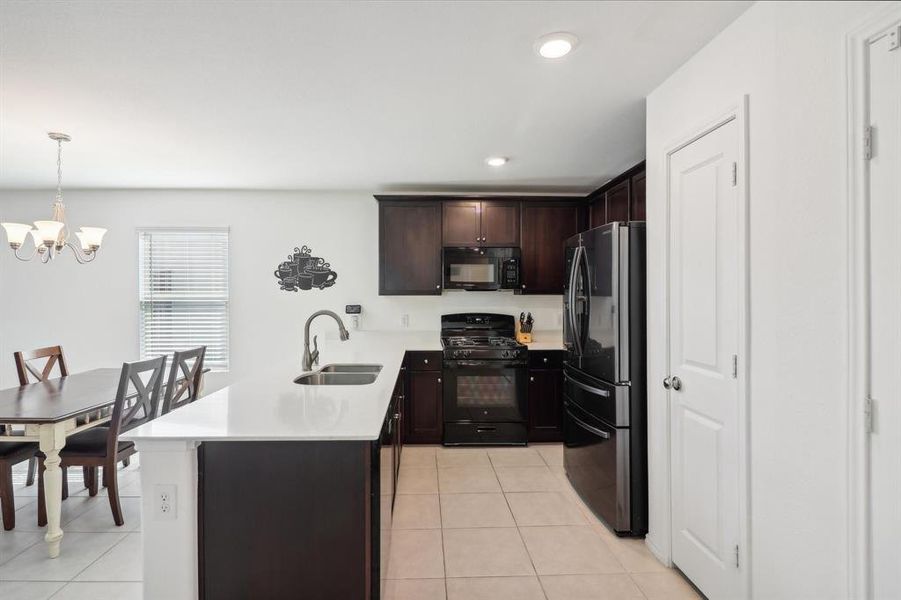 Kitchen featuring light tile patterned flooring, sink, kitchen peninsula, decorative light fixtures, and black appliances