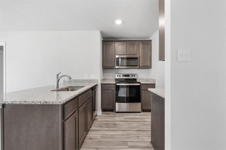 Kitchen featuring light hardwood / wood-style flooring, appliances with stainless steel finishes, sink, kitchen peninsula, and dark brown cabinetry