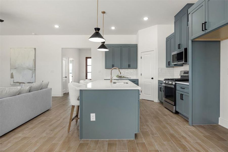 Kitchen featuring light hardwood / wood-style floors, tasteful backsplash, an island with sink, appliances with stainless steel finishes, and sink