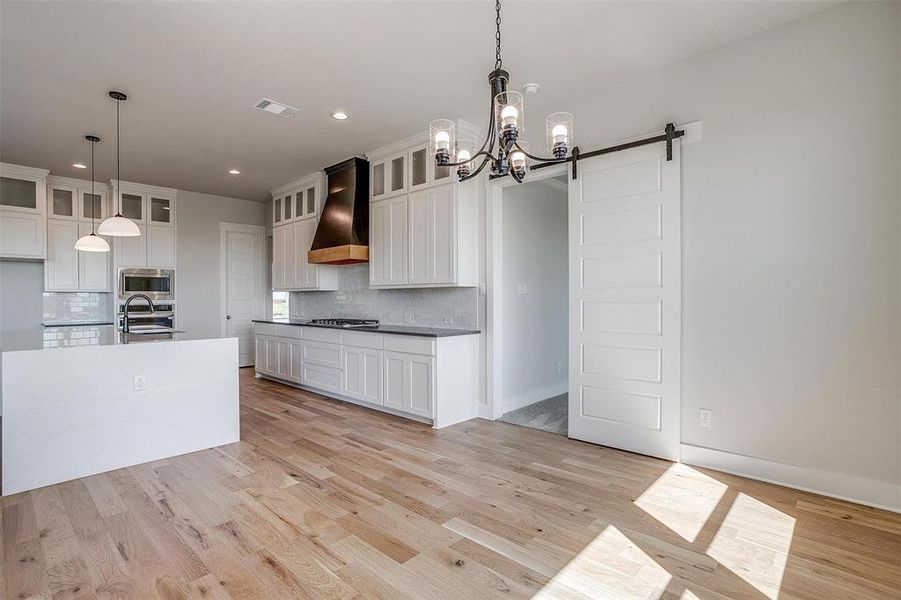 Kitchen featuring custom exhaust hood, stainless steel appliances, pendant lighting, light wood-type flooring, and a barn door