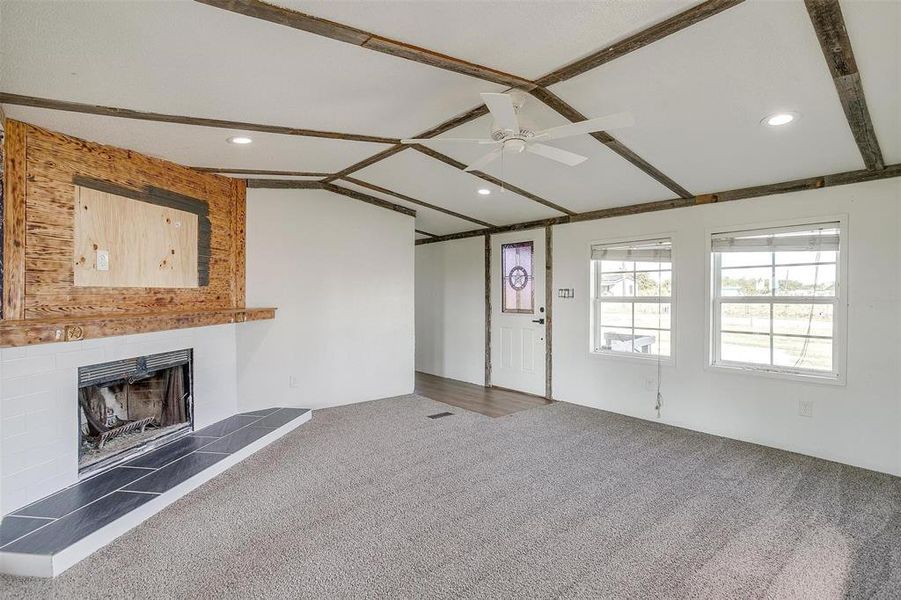 Unfurnished living room with a fireplace, vaulted ceiling, dark colored carpet, and ceiling fan