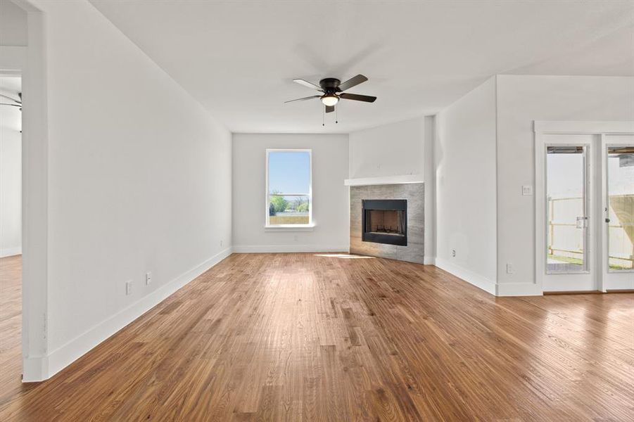 Unfurnished living room featuring hardwood / wood-style floors, ceiling fan, and a tile fireplace