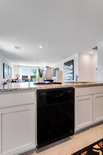 Kitchen featuring white cabinets, sink, black dishwasher, light stone countertops, and light tile patterned floors
