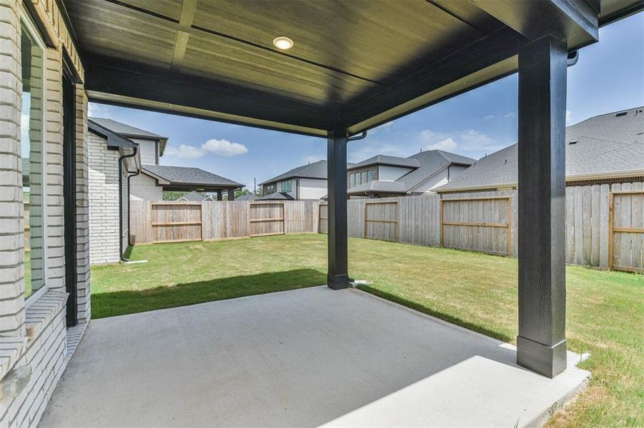 This is a spacious and covered backyard patio with a well-maintained lawn, enclosed by a privacy fence, offering a great outdoor space for relaxation and entertainment.