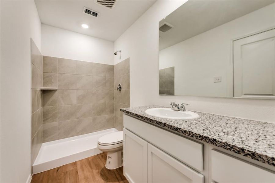 Bathroom with vanity, toilet, a tile shower, and hardwood / wood-style floors