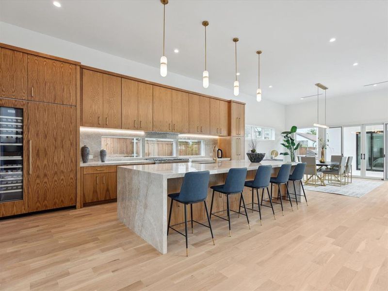 Kitchen featuring light wood-type flooring, a large island, decorative light fixtures, a breakfast bar, and tasteful backsplash