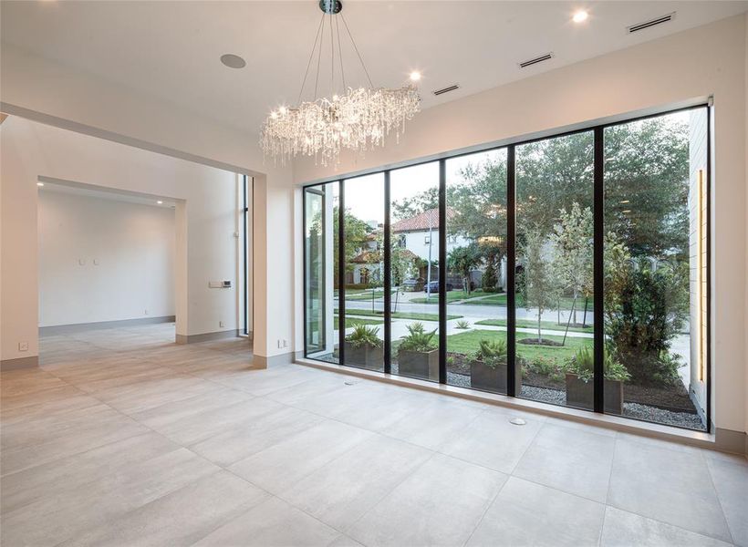 Alternate formal dining room view featuring the sophisticated crystal chandelier and wall of windows radiating natural light and a view embracing the front yard and custom steel planters