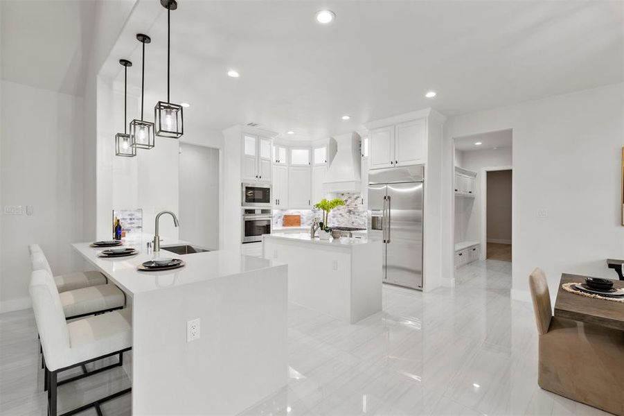 Kitchen with a kitchen island, built in appliances, sink, white cabinets, and kitchen peninsula