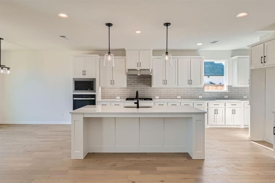 Kitchen featuring white cabinetry, stainless steel oven, pendant lighting, and an island with sink