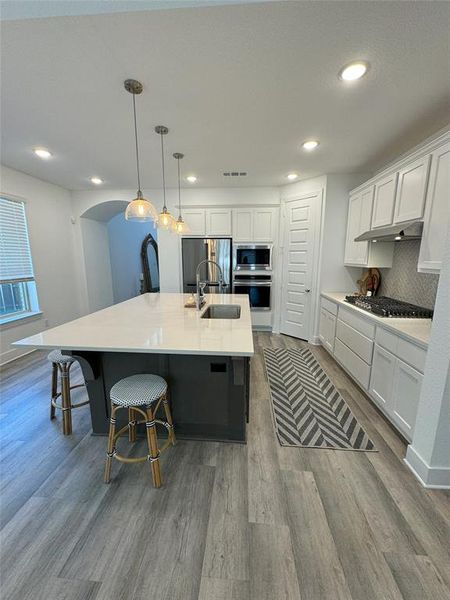 Kitchen featuring white cabinets, appliances with stainless steel finishes, a spacious island, light wood-type flooring, and pendant lighting