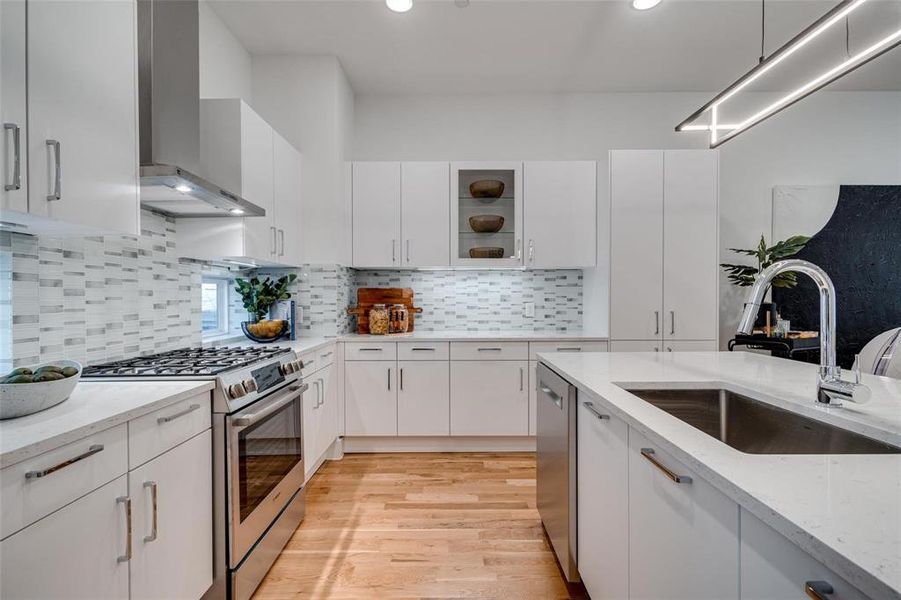 Kitchen with white cabinets, appliances with stainless steel finishes, sink, and wall chimney range hood