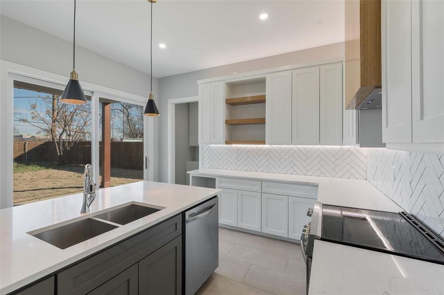 Kitchen with white cabinetry, stove, decorative light fixtures, stainless steel dishwasher, and sink