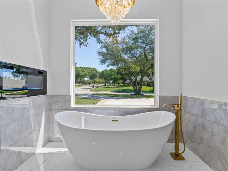 Bathroom featuring a healthy amount of sunlight, a bathing tub, and tile walls