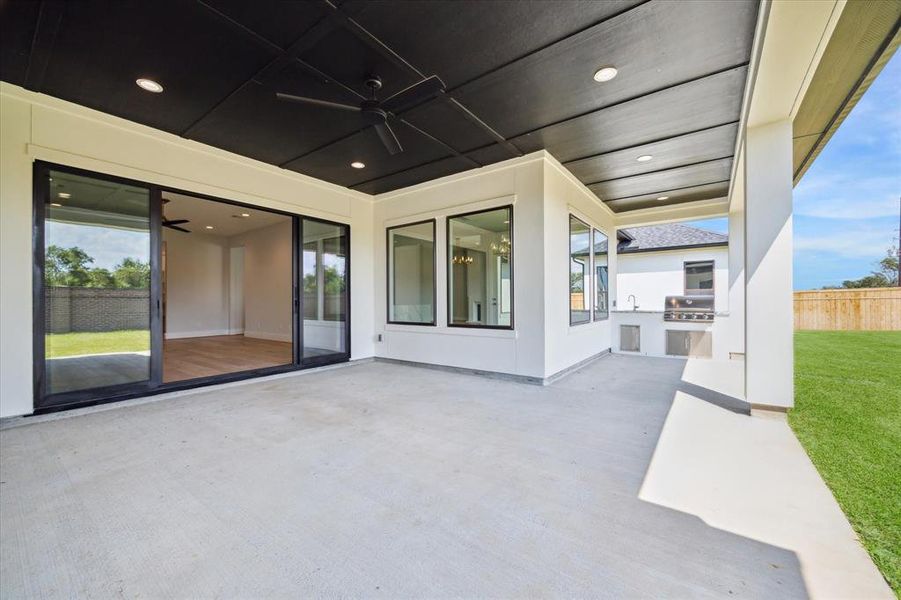 A sliding window wall opens to a spacious covered patio, complete with a summer kitchen. The summer kitchen has a grill, plus a sink and faucet.