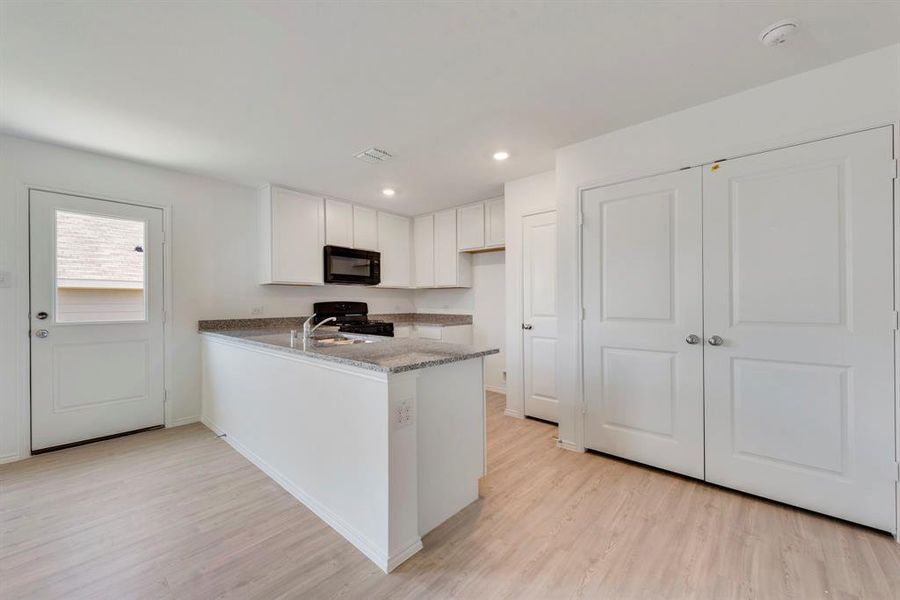 Kitchen featuring light hardwood / wood-style flooring, black appliances, white cabinetry, and kitchen peninsula