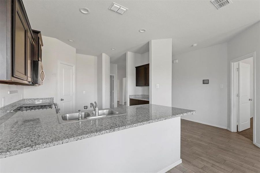 Kitchen with hardwood / wood-style floors, sink, kitchen peninsula, and light stone counters