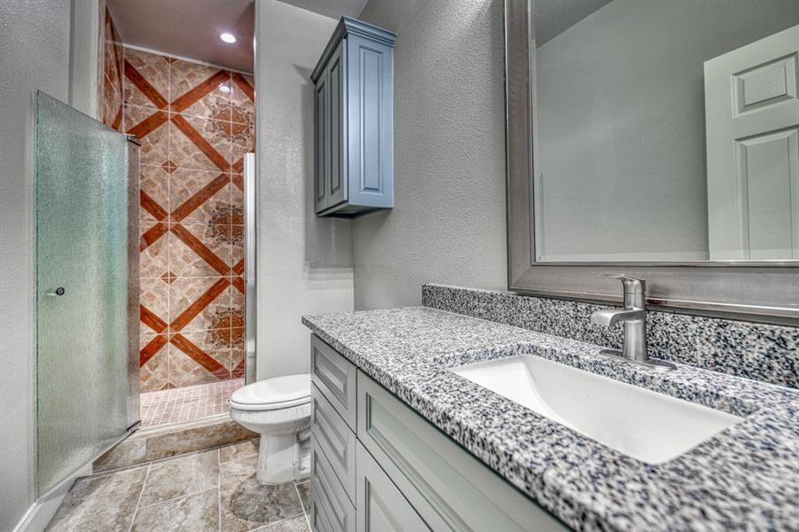 Bathroom featuring tiled shower, tile flooring, large vanity, and toilet