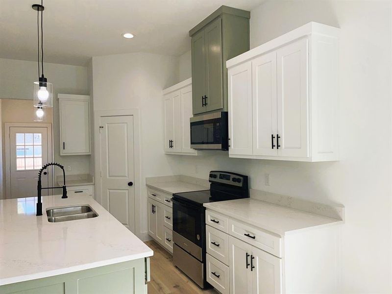 Kitchen with light stone countertops, sink, light hardwood / wood-style floors, stainless steel appliances, and pendant lighting