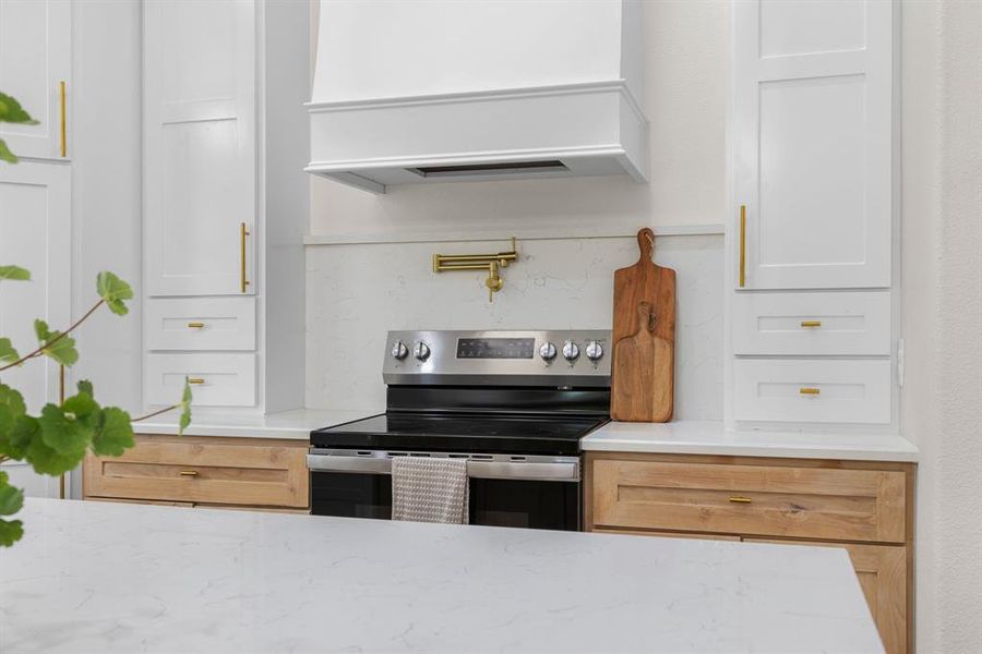Kitchen featuring light stone counters, premium range hood, stainless steel electric range, and white cabinets