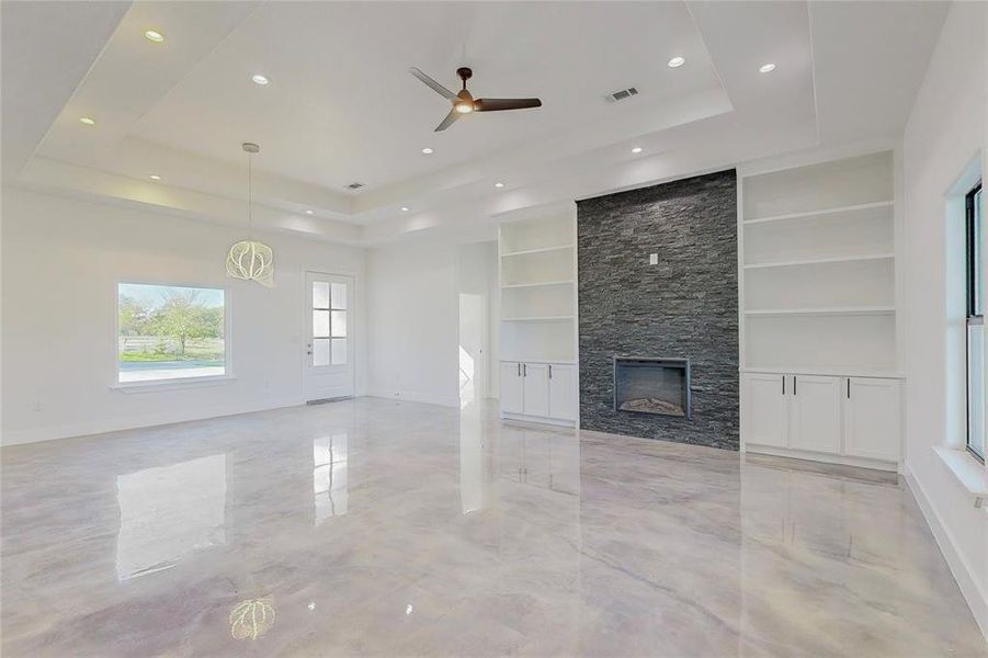 Unfurnished living room featuring a stone fireplace, built in features, and a tray ceiling