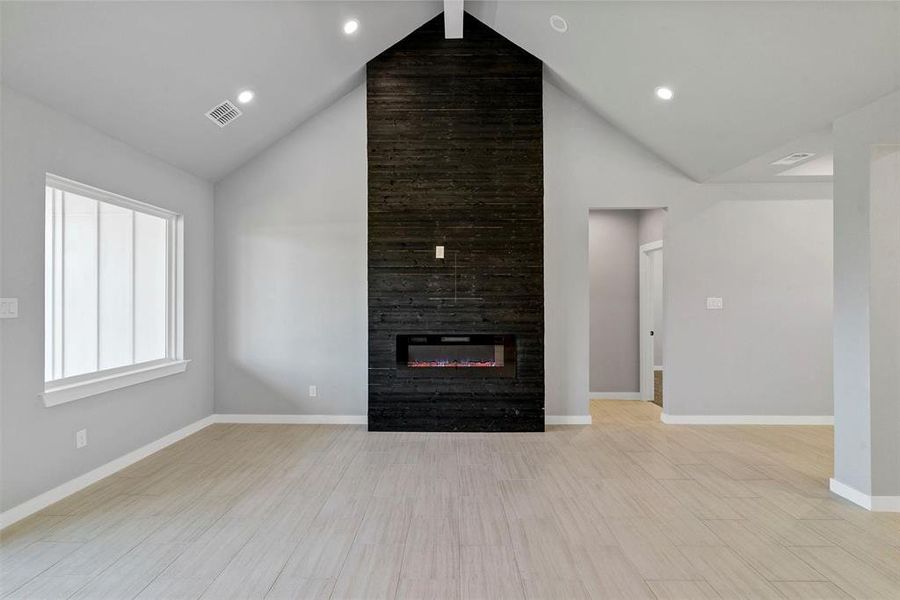 Unfurnished living room with beamed ceiling, light hardwood / wood-style flooring, a tiled fireplace, and high vaulted ceiling