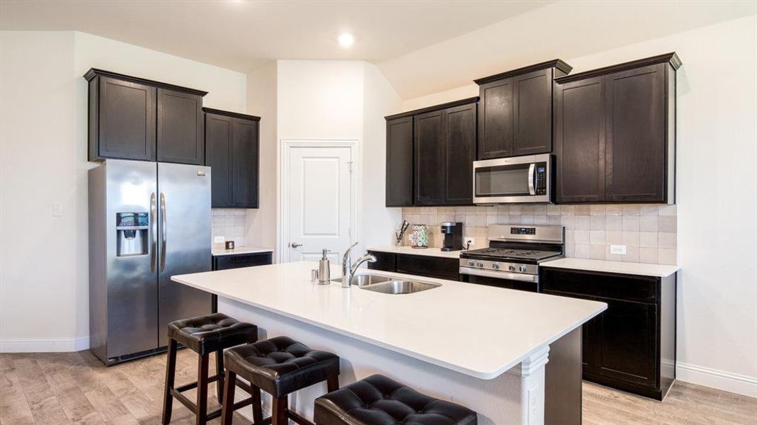 Kitchen with stainless steel appliances, tasteful backsplash, a kitchen island with sink, and light wood-type flooring