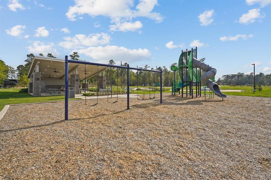 This community playground features swings and a slide, with a covered picnic area in the background, in a well-maintained park with open green spaces is just a few steps from the property.