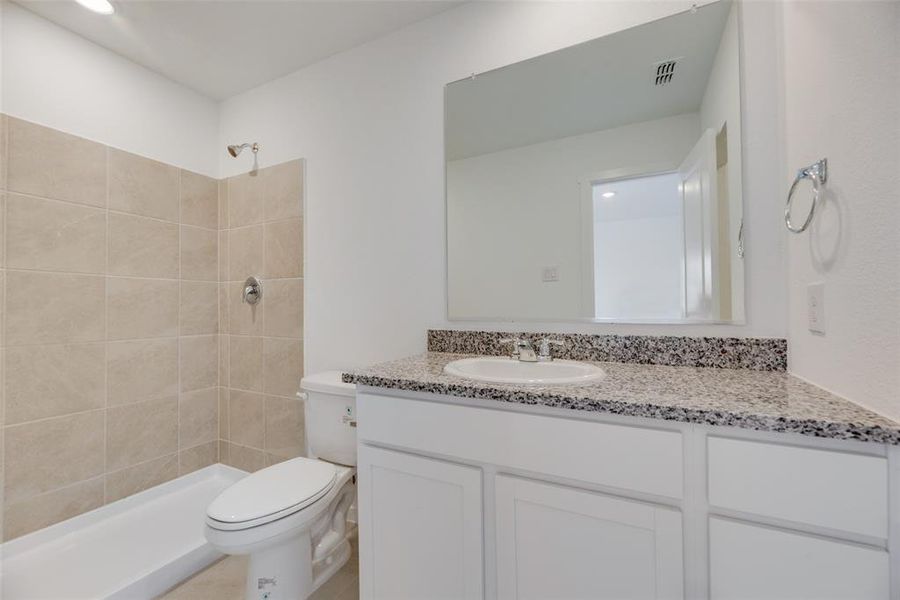 Bathroom featuring vanity, a tile shower, and toilet